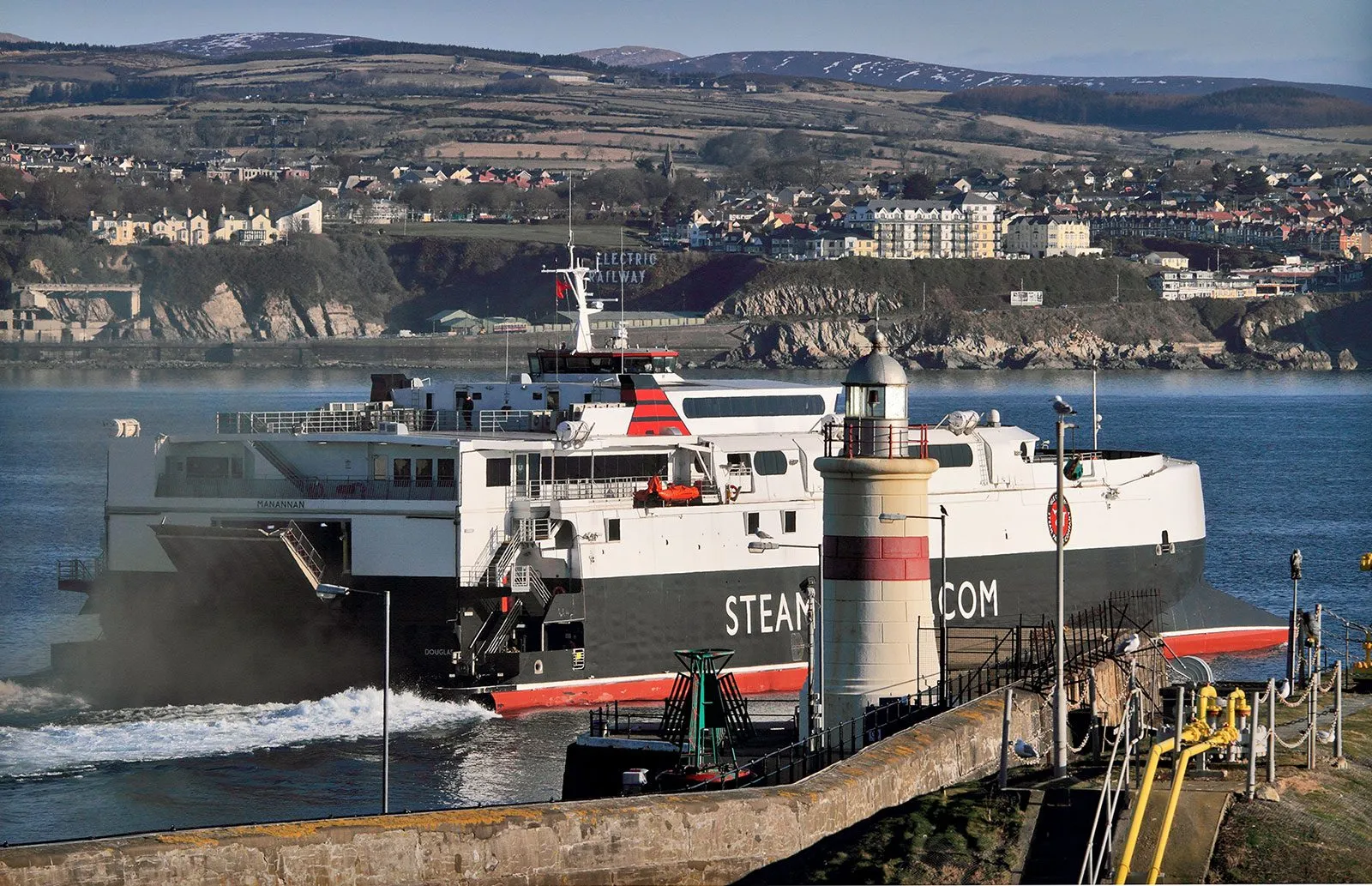 The Steam Packet fast craft Manannan leaving Douglas harbour past the lighthouse, with houses on the hillside behind