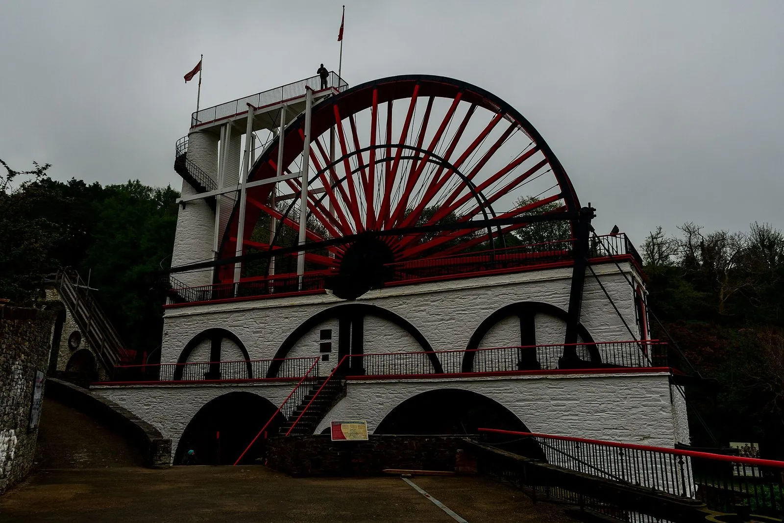 The Great Laxey Wheel, painted red and white, with its viaduct and spiral staircase in the wooded valley above Laxey