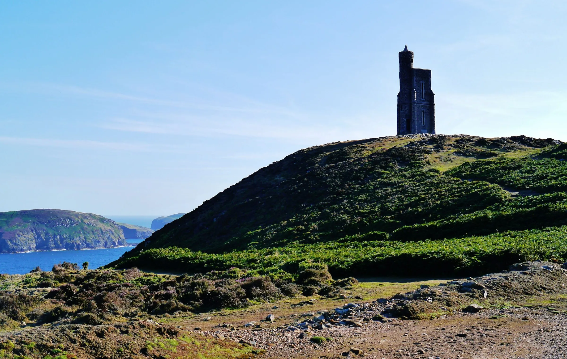 Milner's Tower on the heather-covered summit of Bradda Head above Port Erin, with the sea and the south-west coast behind under a clear blue sky