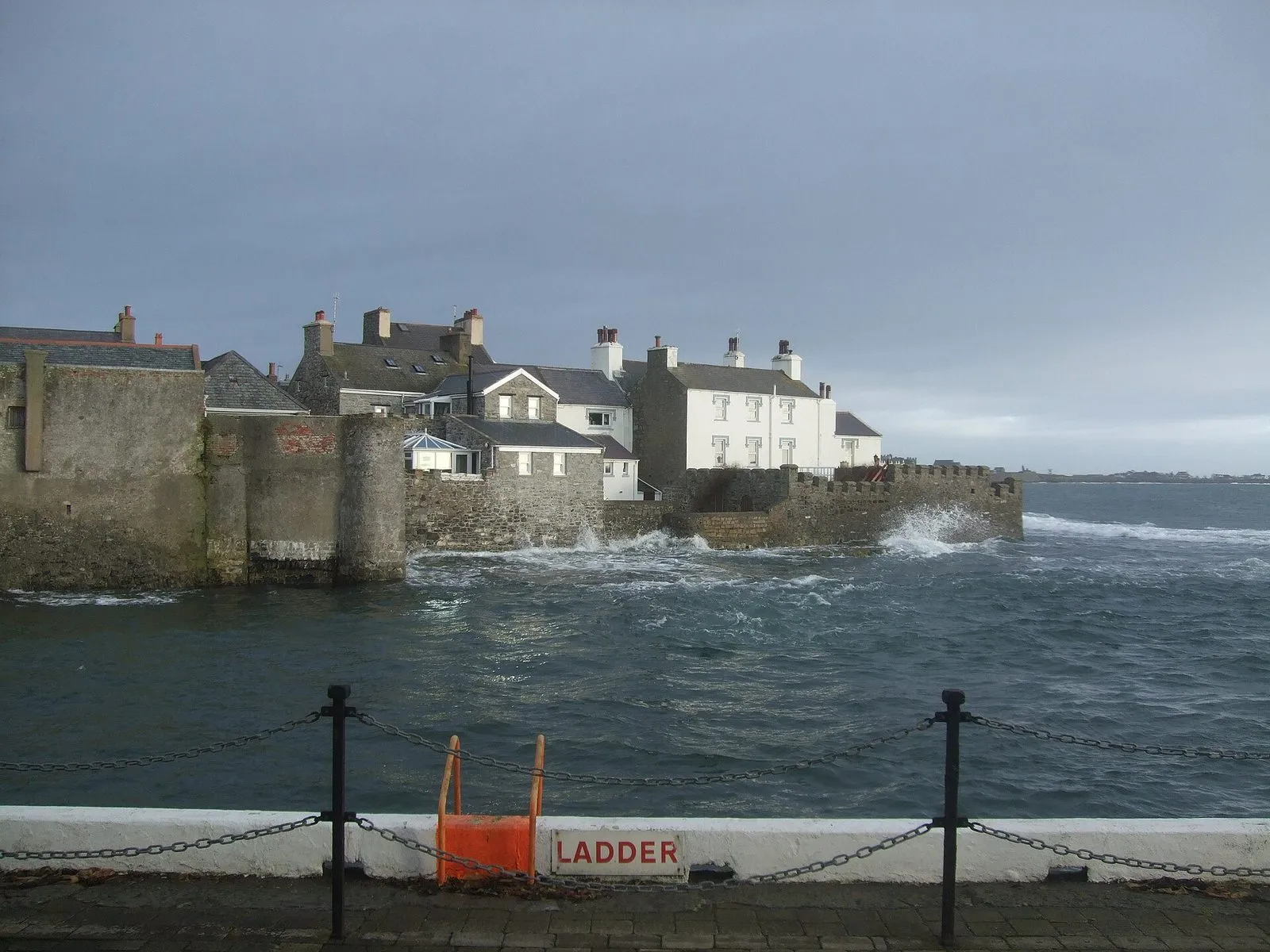 Whitewashed stone cottages on the harbour wall at Castletown, with waves breaking on the sea wall below a grey sky