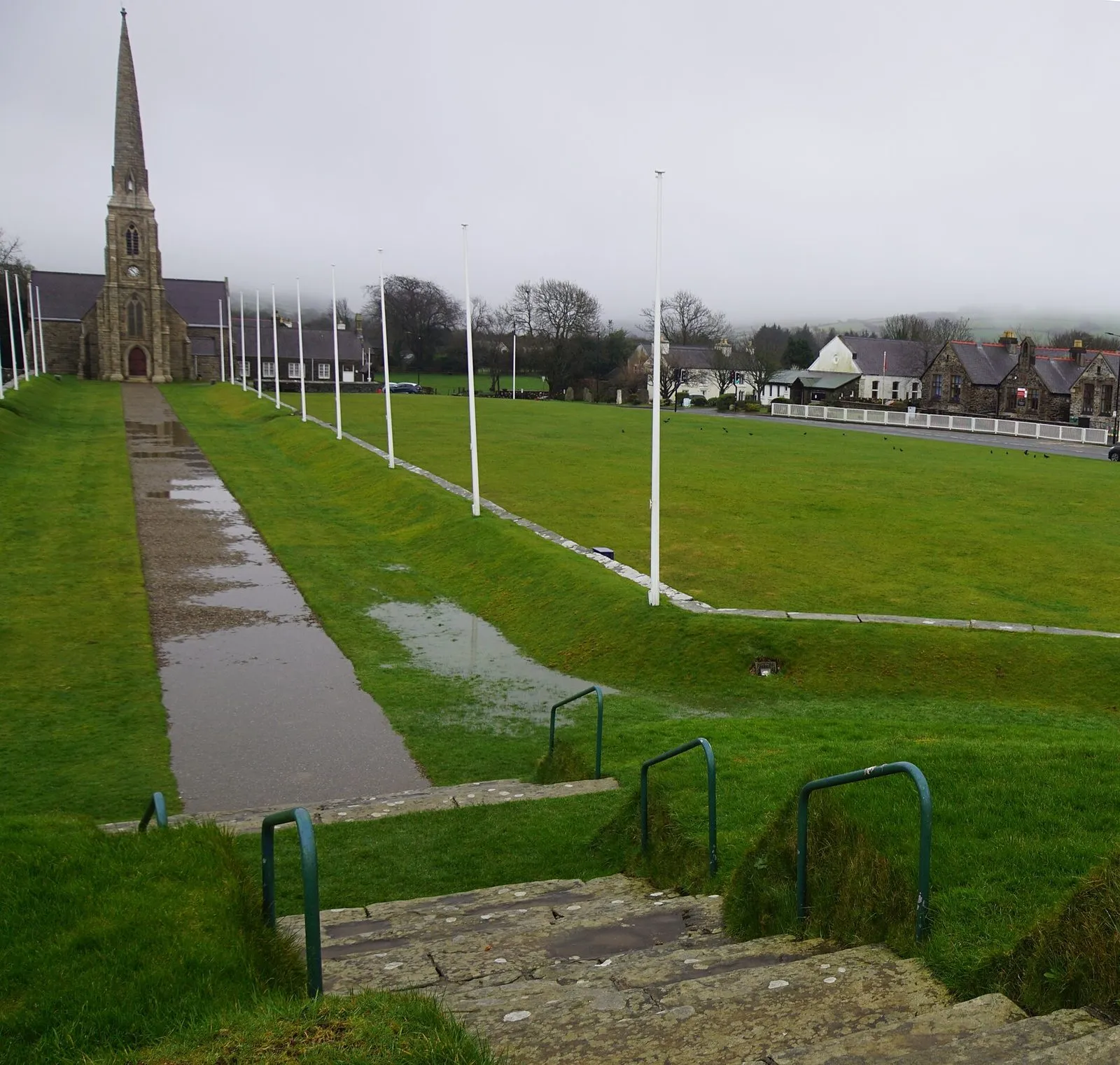 The long straight processional path running from the stone steps of Tynwald Hill across wet green grass to St John’s Chapel and its tall spire, lined with white flagpoles