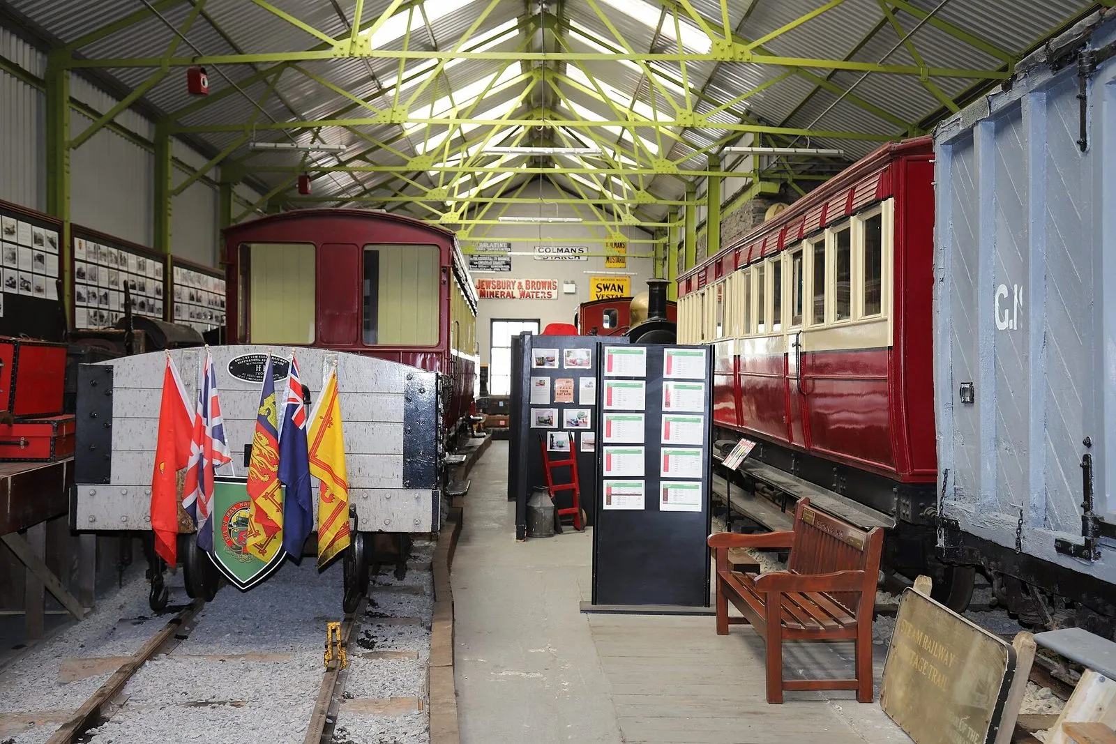 Inside the Port Erin railway museum: red carriages and an old wagon on short tracks under a green steel roof, with display boards between them
