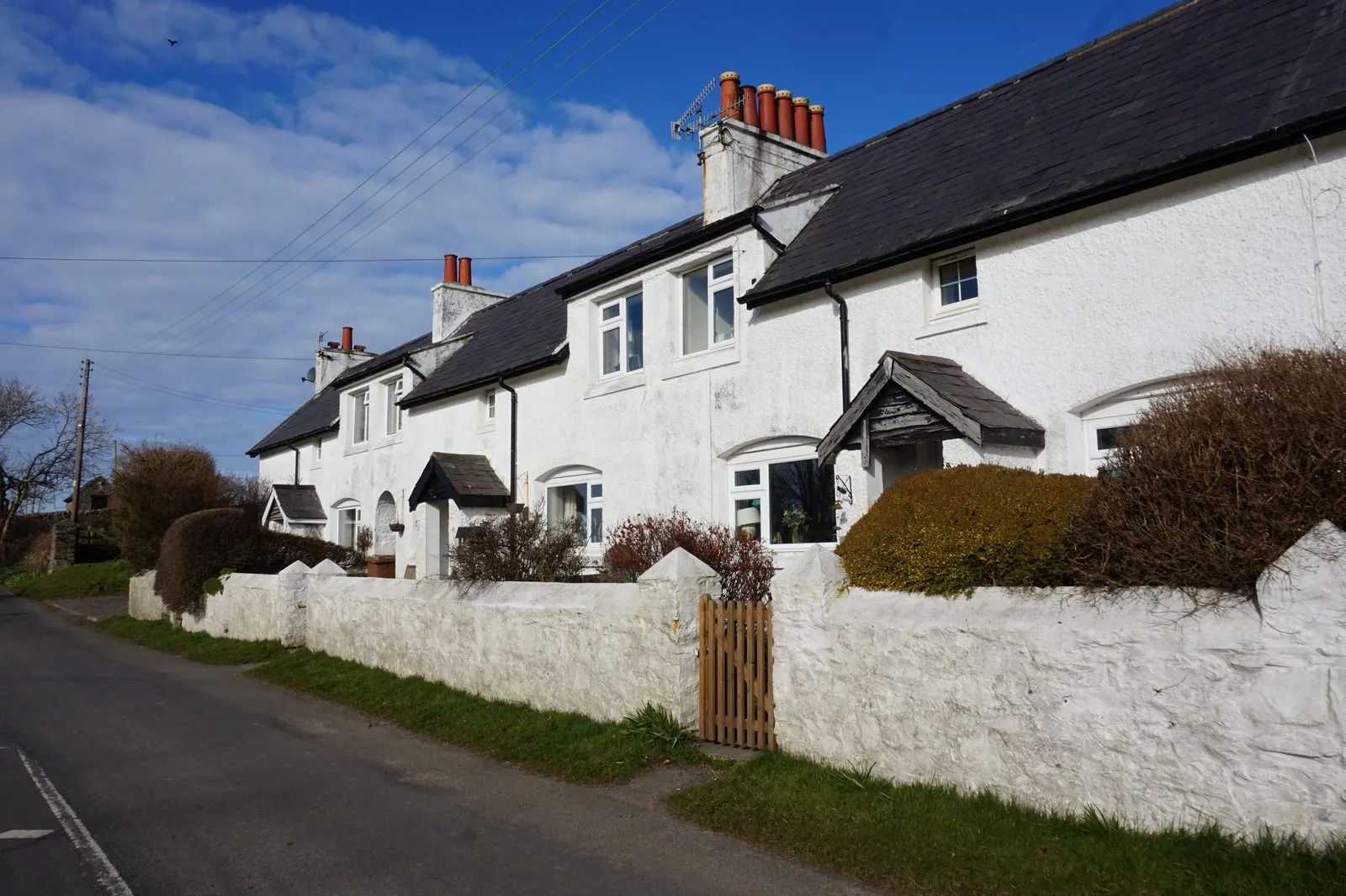 A terrace of whitewashed cottages with slate roofs and red chimney pots behind a white stone wall on a country road