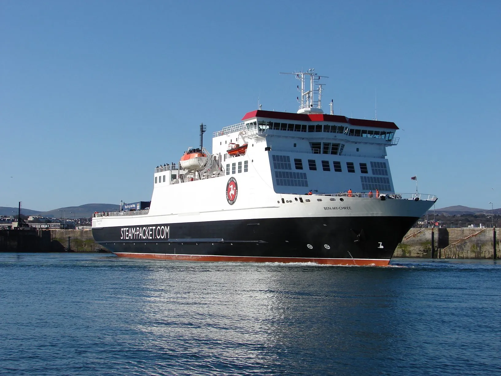 The Steam Packet ferry Ben-my-Chree, white with a black hull and red funnel top, sailing into Douglas harbour under a clear blue sky