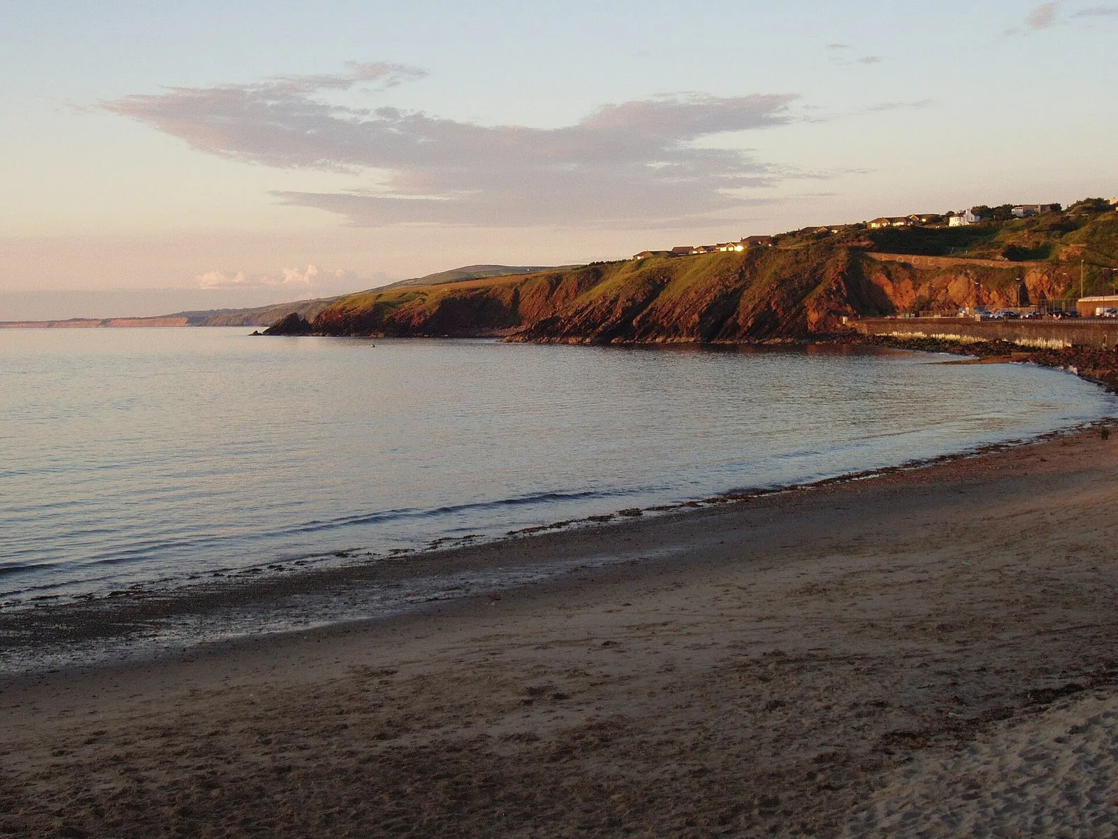 Peel beach and the red sandstone cliffs of the bay glowing pink and orange in evening sun, with calm water