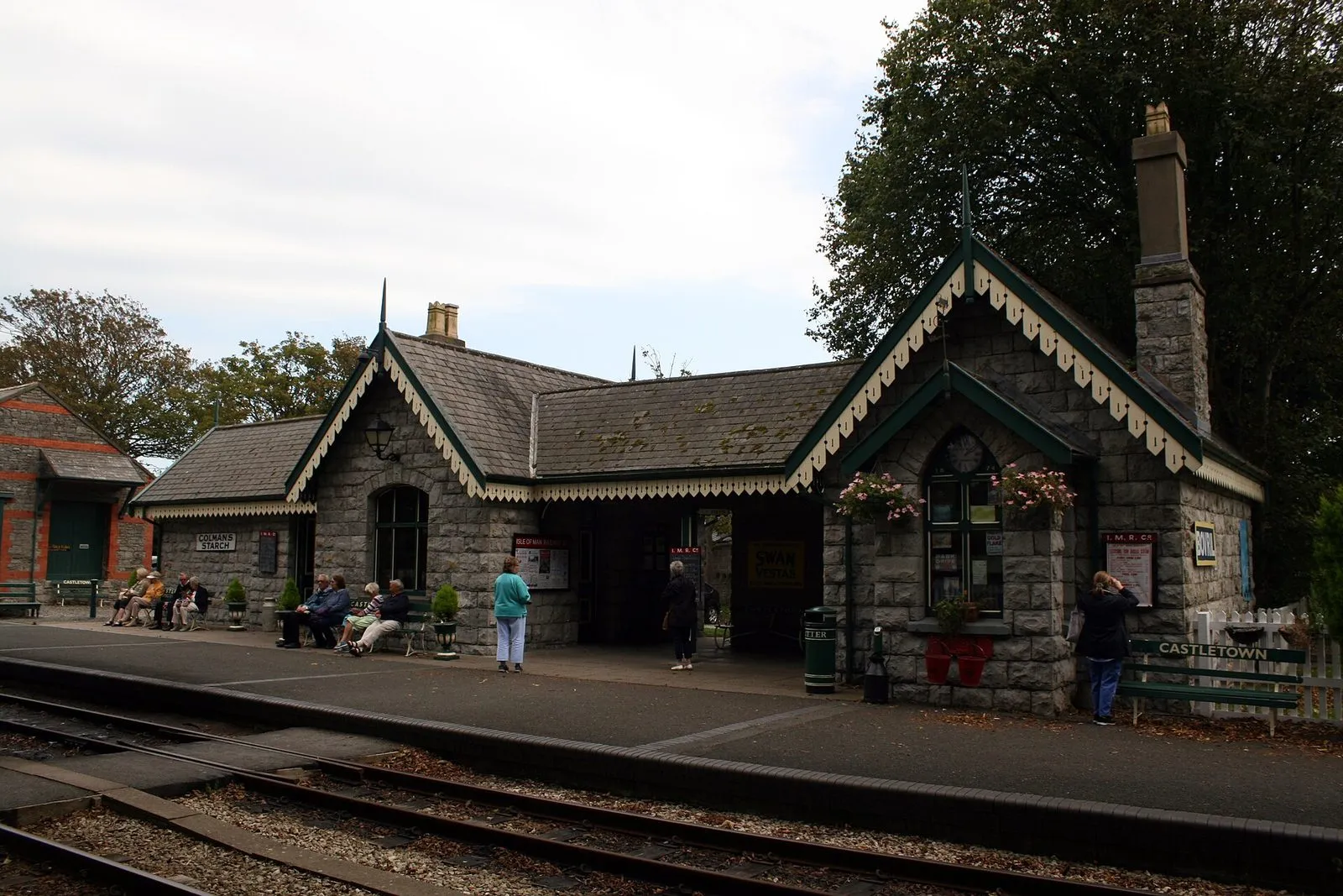 The stone Castletown railway station building with green-painted gables, flower baskets and a platform beside the tracks